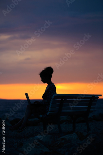 woman with laptop on evening beach