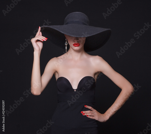 Luxury woman in a large black hat and bright lips on black background