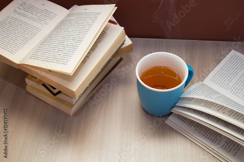 a stack of books and a hot drink in a blue mug on wooden table,