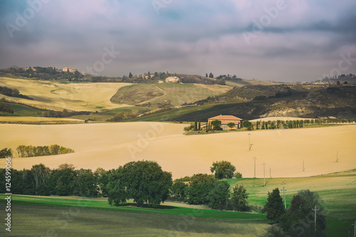 Wavy fields in Tuscany with shadows and farms, Italy. Natural outdoor seasonal summer background with blue sky and clouds.