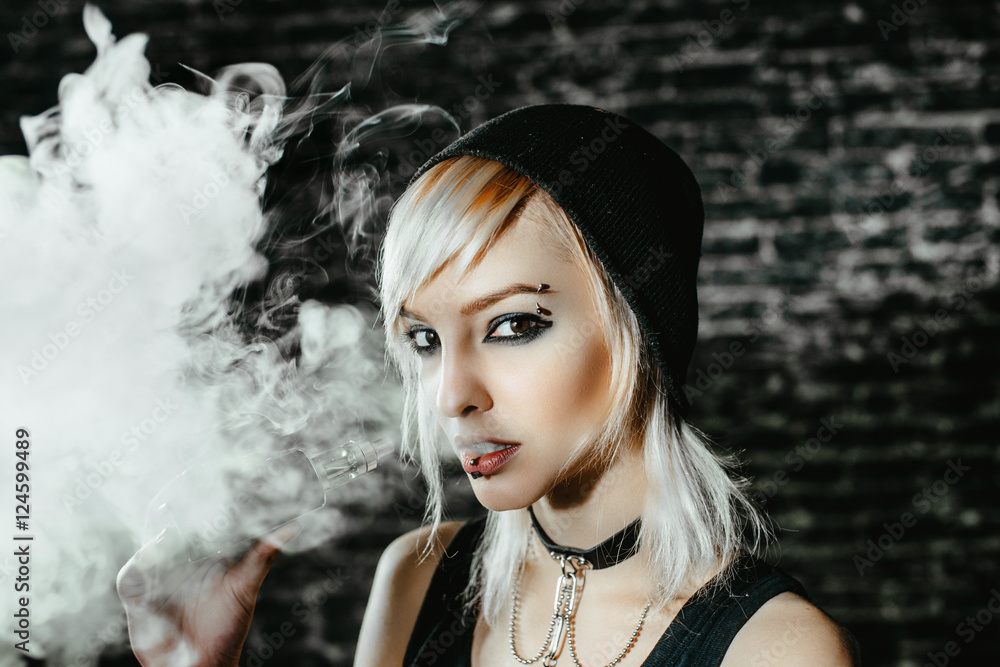 Sexy goth girl smokes electronic cigarette on dark background. The model  vaper vaping a vaporizer in the studio. foto de Stock | Adobe Stock