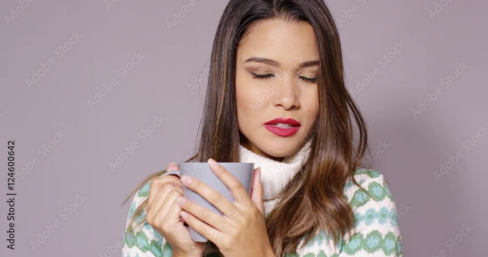 Attractive young woman in a stylish winter jersey enjoying a hot beverage in a large cup looking into the distance with a dreamy expression Attractive young woman in a stylish winter jersey enjoying a hot beverage in a large cup looking into the distance with a dreamy expression