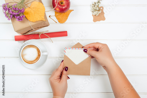 Female hands hold gift card. Gift boxes, cup of cappuccino on autumn background. photo