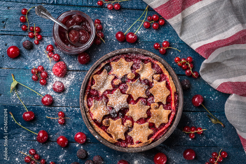 Berry pie decorated with stars, jam, sugar powder and berries on the navy-blue background with kitchen towel