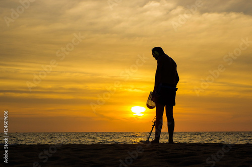 Treasure hunter with Metal detector on the sunset the beach