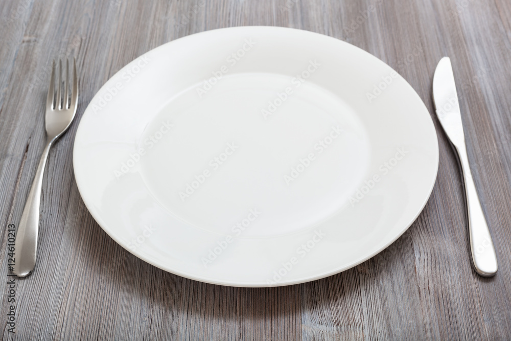 white plate, knife, spoon on gray brown table white plate, knife, spoon on gray brown table