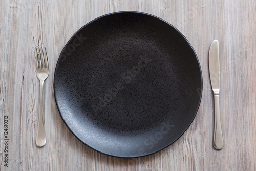 top view of black plate with knife, spoon on gray