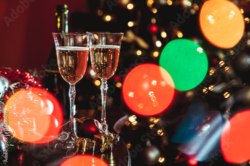 Christmas still life - Two glasses of champagne with Xmas decorations and Christmas tree on blurred background red room
