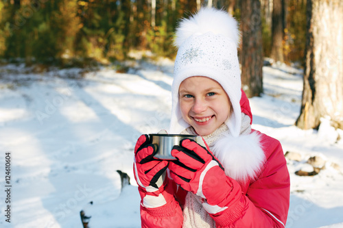 Child drinking tea in thermos mug in forest with snow, winter hi photo