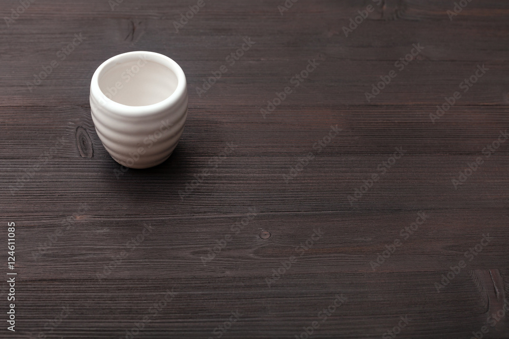 white cup for sake on dark brown wooden board white cup for sake on dark brown wooden board