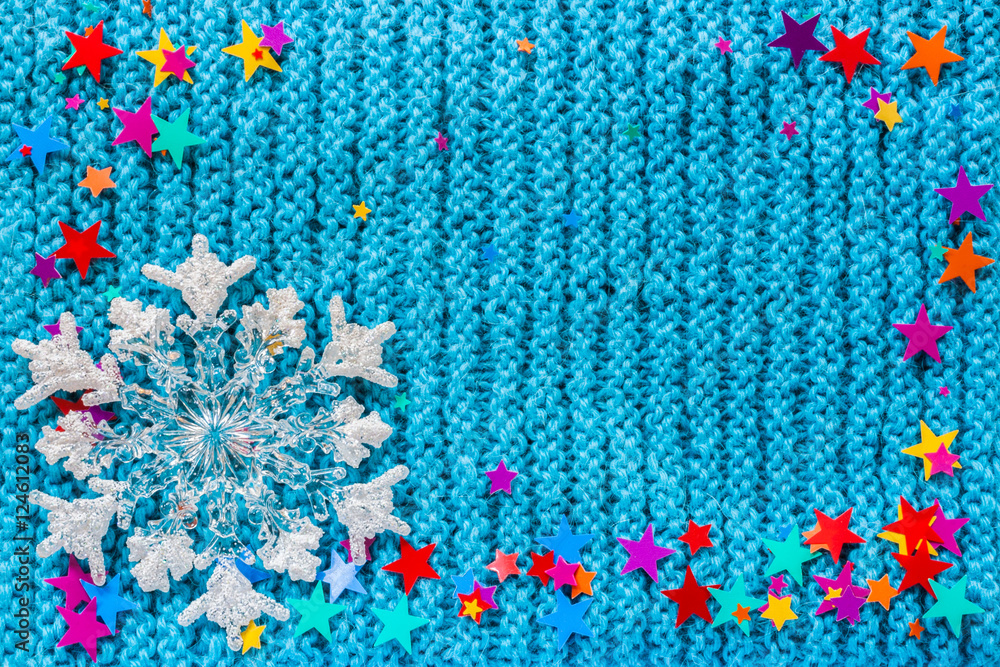 White snowflake and multicolor stars on a blue knit background.