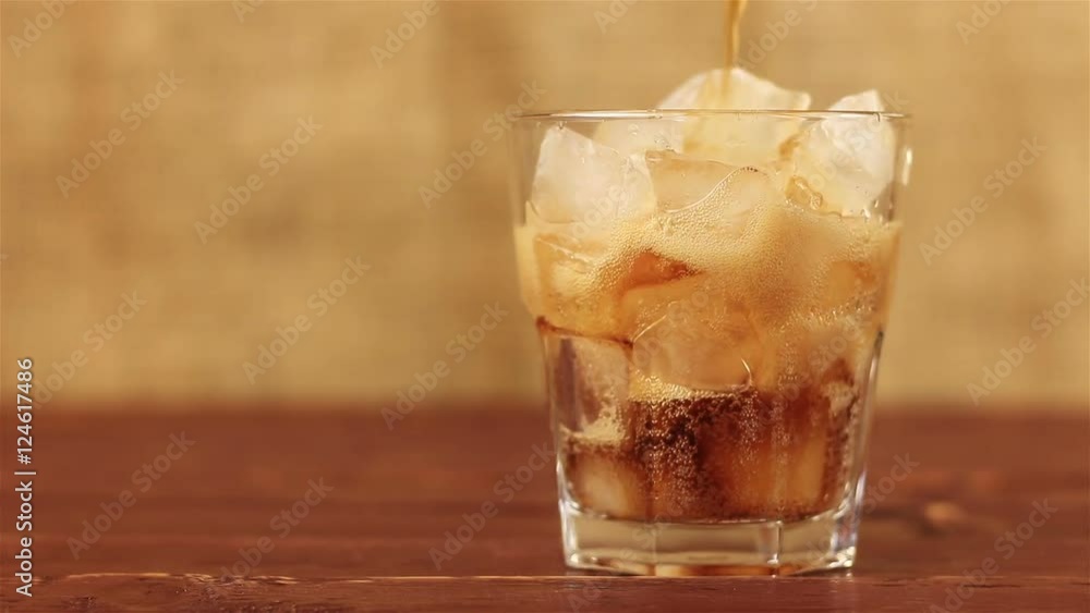 Cola with ice. Pouring Cola with Ice and bubbles in glass on a wooden table and brown background Cola with ice. Pouring Cola with Ice and bubbles in glass on a wooden table and brown background