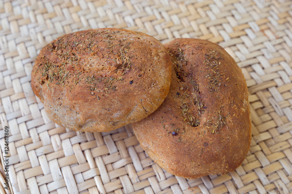 Two loaves of rye bread round shape. Bread strewing herbs on the table made from natural materials