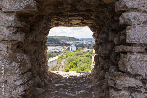 Old windmill through small window in fortress wall, Obidos