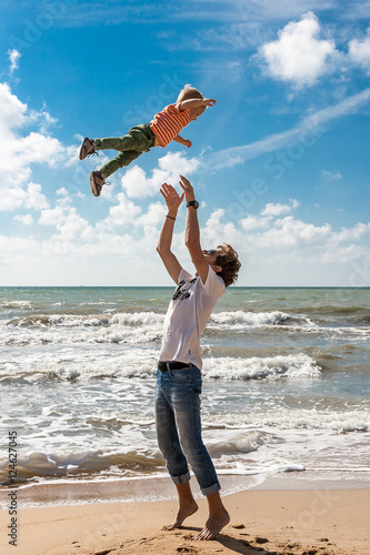 The elder brother throws his younger  on the beach against the backdrop of the sea. Happy carefree childhood