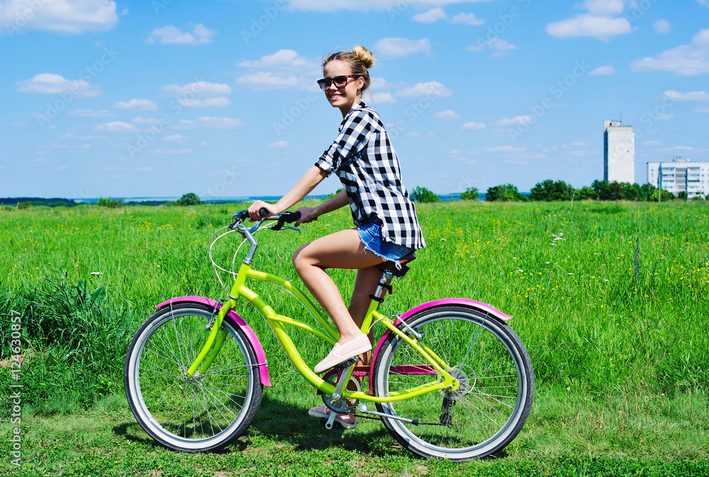 Beautiful girl riding bicycle outdoors across the green sunny field Beautiful girl riding bicycle outdoors across the green sunny field