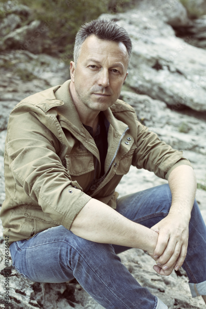 Obraz premium Outdoor male portrait. Handsome middle-aged man sitting on rocks