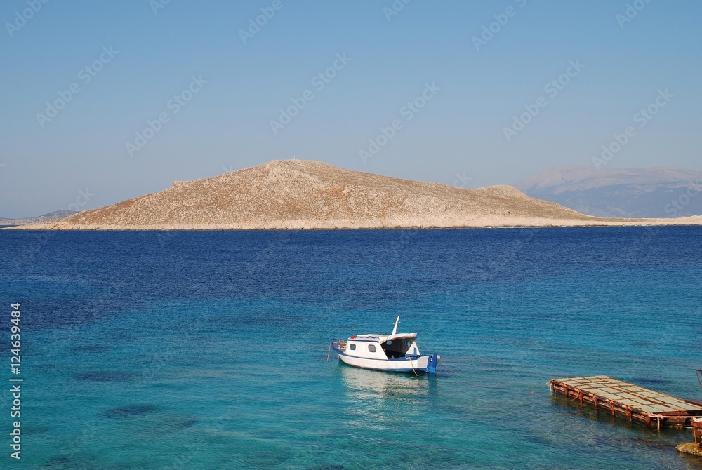 A small boat moored near Ftenegia beach at Emborio on the Greek island of Halki. The uninhabited island of Nissos is in the background.