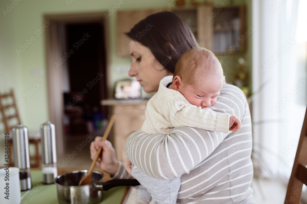 Young mother in kitchen holding baby son, cooking Young mother in kitchen holding baby son, cooking