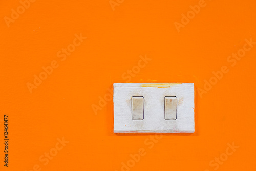 Close-up detail of a pair of white switches on a vibrantly colored orange wall. Interior design concept and background.