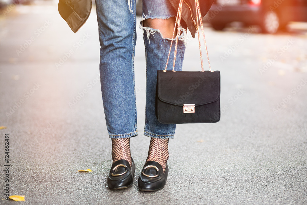 fall outfit fashion details, young stylish woman wearing ripped jeans and black  loafers. fashion blogger holding a trendy black purse with a golden chain.  Stock Photo | Adobe Stock