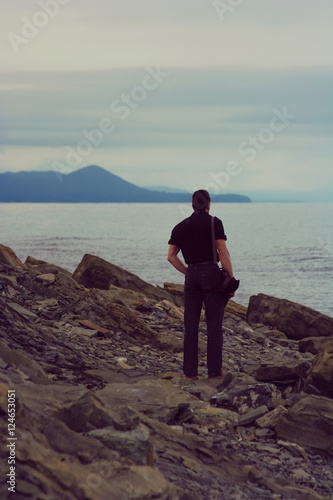 Back view portrait of man standing on a seashore in a cloudy weather, feeling of loneliness and sadness © Sonate