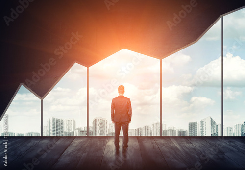 Slika na platnu Businessman standing on the floor back to us looking through the big window with cityscape and sunset behind it