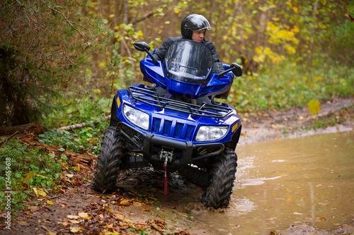 Man is riding an ATV through an autumn wood.