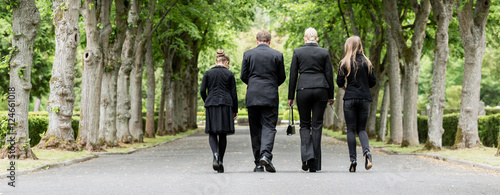 Familie läuft auf Allee im Friedhof in Trauer mit Blumen in der Hand