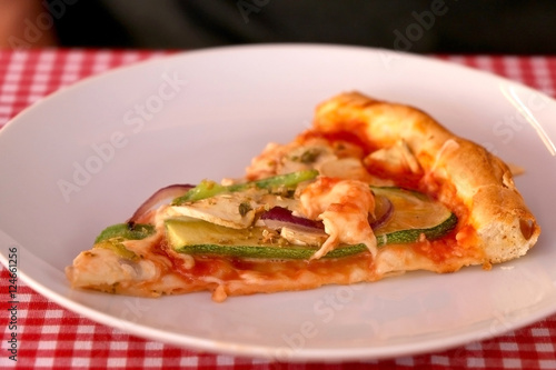 Slice of vegetarian pizza with cheese, tomato sauce, green peppers, mushrooms and onion in a pizzeria. Selective focus. 