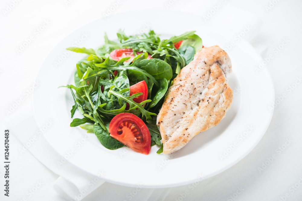 Roasted chicken breast and fresh salad with tomato and greens (spinach, arugula) close up on white wooden background. Healthy food. Roasted chicken breast and fresh salad with tomato and greens (spinach, arugula) close up on white wooden background. Healthy food.