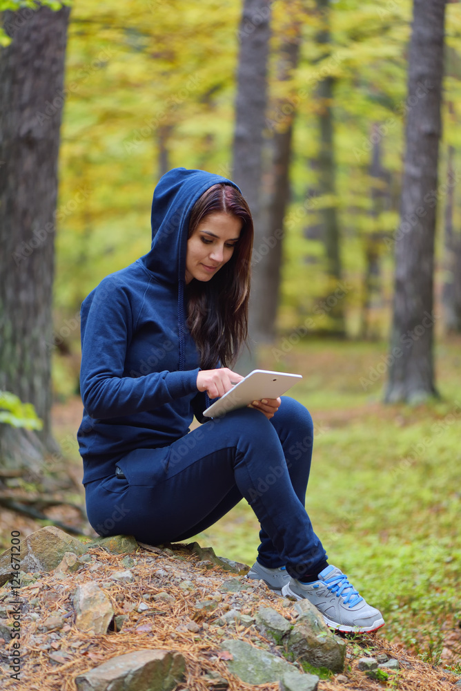 Beautiful happy young woman surfing the web and reading on a tablet in autumn forrest environment Beautiful happy young woman surfing the web and reading on a tablet in autumn forrest environment