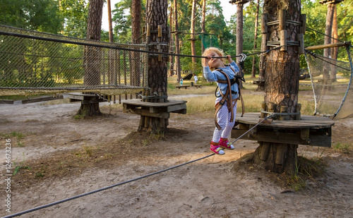 Little girl overcomes obstacles. / Three-year girl the blonde with a personal fall arrest system obstacle in the rope town.