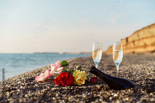 Bottle of champagne, two glasses and rose flowers on the beach. in Greece