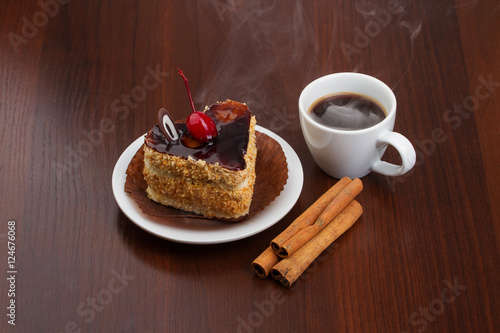 Hot coffee with cinnamon sticks and cake on a plate
