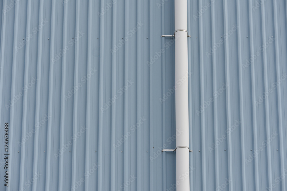 Plastic white rain water pipe attached to tall wall made of gray painted corrugated sheet metal. Plastic white rain water pipe attached to tall wall made of gray painted corrugated sheet metal.