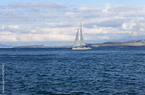 White yacht gliding through a blue bay © ombre spagla