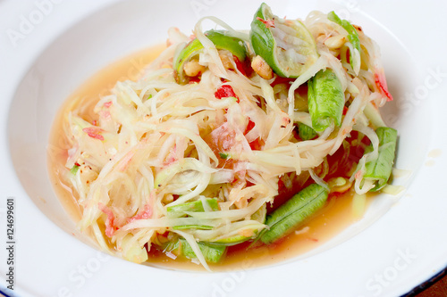 Green Papaya Salad (Som tum Thai) in white dish on wood table, Thai cuisine spicy delicious