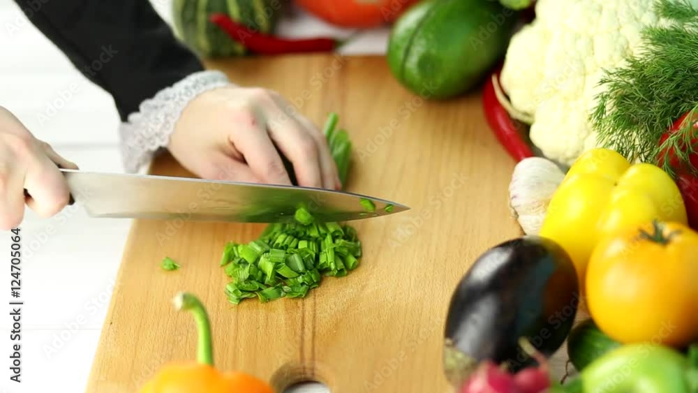 Woman cuts green onions among the fresh vegetables Woman cuts green onions among the fresh vegetables