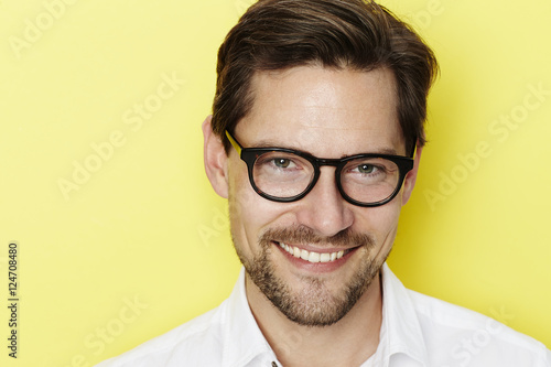 Fototapeta Naklejka Na Ścianę i Meble -  Smiling glasses man in yellow studio