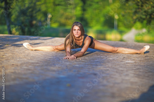 Cute girl makes sports exercises on the nature background. She wore a black kombidress body.She sits facing us. she is sitting on the splits