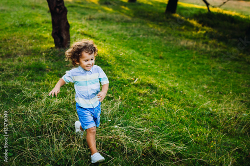 Cute little boy walking in a green park alone