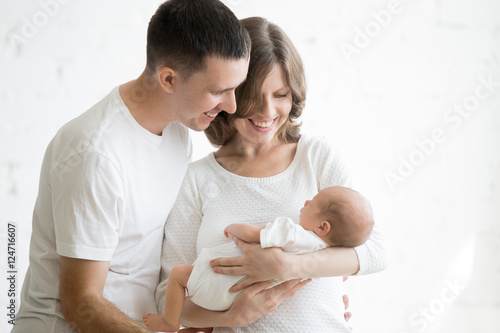 Tableau sur toile Portrait of young happy man and woman holding newborn cute babe dressed in white unisex clothing