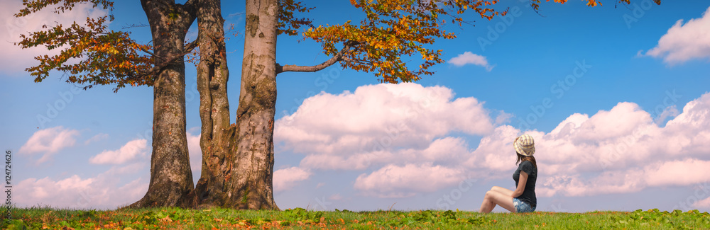 Obraz premium Woman sitting under the tree on a green hill