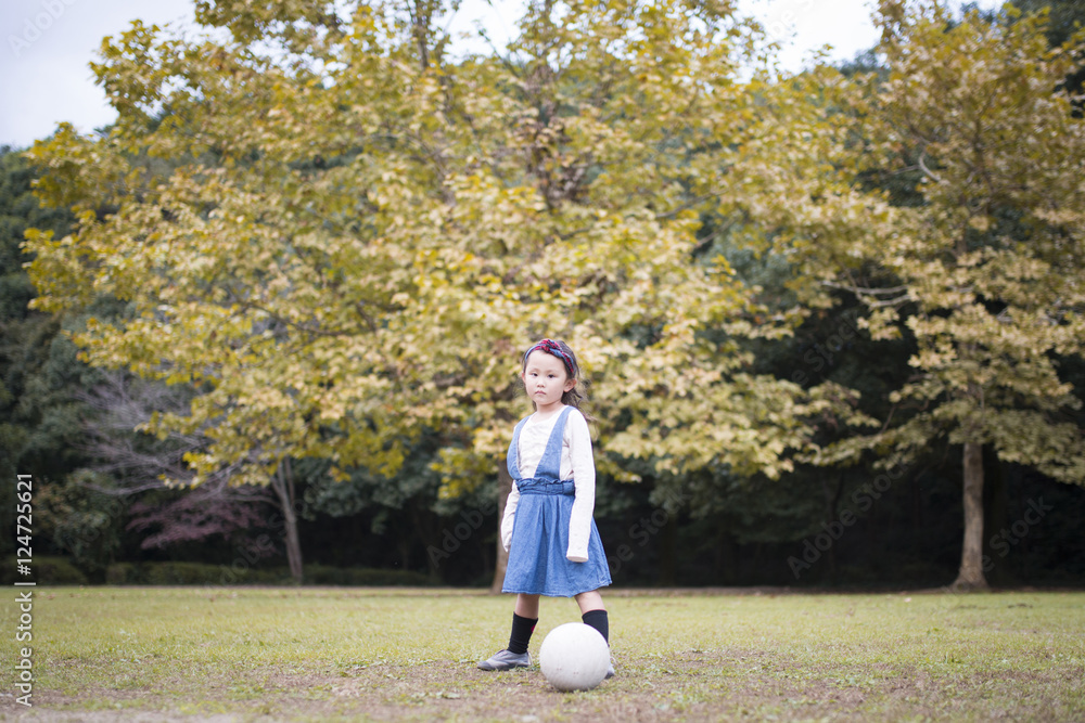 秋の公園でサッカーボールで遊ぶ女の子