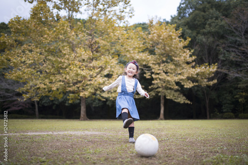 秋の公園でサッカーボールで遊ぶ女の子