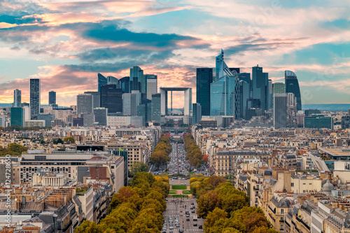 La Defense Financial District Paris France in autumn. Traffic on Champs-Elysees with orange and yellow trees aside. Modern vs. Old architecture. Sunset bright sky.
