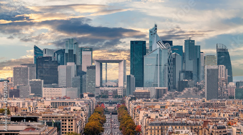 La Defense Financial District Paris France in autumn. Traffic on Champs-Elysees with orange and yellow trees aside. Modern vs. Old architecture. Sunset sky with clouds.