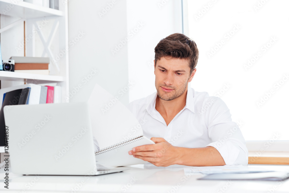Handsome businessman sitting at the desk and using laptop Handsome businessman sitting at the desk and using laptop
