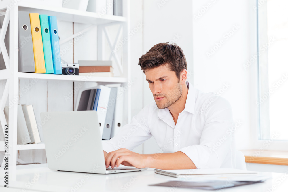 Young thoughtful handsome businessman sitting at the table with laptop